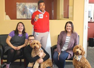 State Farm agent offers insurance plus puppy love! Surrounding a cardboard cutout of “Jake,” State Farm Insurance’s chief advertising spokesperson, are Mark Creevey’s office “staff,” (from left) Gillian Moreno, Creevey holding his golden-doodle Willow, Sarah Kimsey-Sauro and visiting golden-doodle Olive.