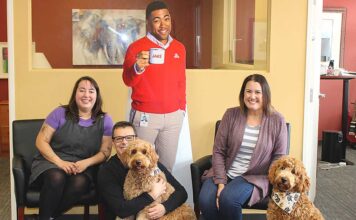 State Farm agent offers insurance plus puppy love! Surrounding a cardboard cutout of “Jake,” State Farm Insurance’s chief advertising spokesperson, are Mark Creevey’s office “staff,” (from left) Gillian Moreno, Creevey holding his golden-doodle Willow, Sarah Kimsey-Sauro and visiting golden-doodle Olive.