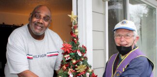 Meals On Wheels People volunteer driver Bill Gerkin (right) hands a Christmas tree to Donald Daniel.