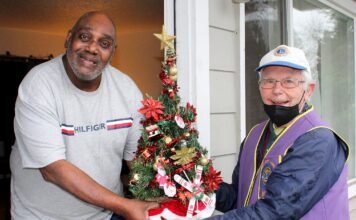 Meals On Wheels People volunteer driver Bill Gerkin (right) hands a Christmas tree to Donald Daniel.