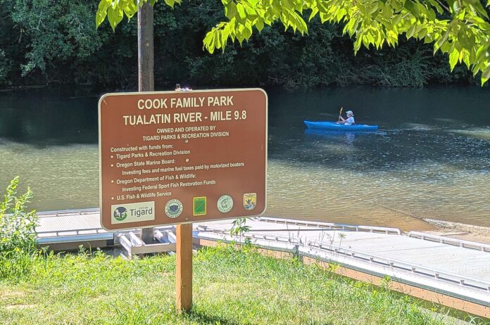 Sign for the Cook Family Park boat launch on the Tualatin River with a kayaker in the background.
