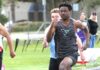 Tigard track hits ground running to start spring Tigard track athlete Marcus Burton, wearing a grey tiger-striped jersey, sprinting at full speed during a 100-meter dash on an outdoor track.