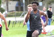 Tigard track hits ground running to start spring Tigard track athlete Marcus Burton, wearing a grey tiger-striped jersey, sprinting at full speed during a 100-meter dash on an outdoor track.