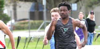 Tigard track hits ground running to start spring Tigard track athlete Marcus Burton, wearing a grey tiger-striped jersey, sprinting at full speed during a 100-meter dash on an outdoor track.