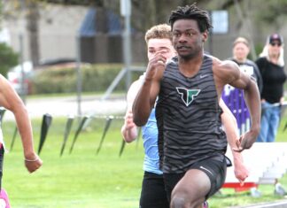 Tigard track hits ground running to start spring Tigard track athlete Marcus Burton, wearing a grey tiger-striped jersey, sprinting at full speed during a 100-meter dash on an outdoor track.
