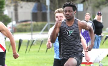 Tigard track hits ground running to start spring Tigard track athlete Marcus Burton, wearing a grey tiger-striped jersey, sprinting at full speed during a 100-meter dash on an outdoor track.