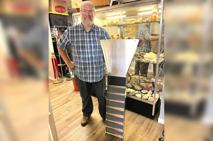 Prospector's-Treasure-Trove Dan Rouse, owner of Prospector's Treasure Trove, stands with a sluice box in front of a display case showing gold-mining artifacts in his store.