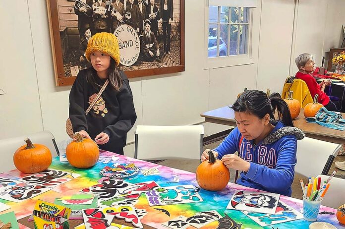 Two people carving pumpkins at a table.
